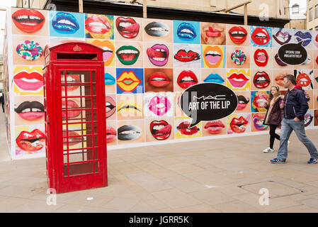 Großen Plakatwand auf UK High Street voller Mund mit Lippenstift neben einer roten Telefonzelle Werbung MAC Cosmetics, stilisiert als M· FRIEDRICH C, ein Kosmetik-Herstellung Stockfoto