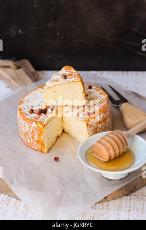 Französischer Weichkäse mit Orangenschale auf Wachspapier, roten Pfefferkörnern, Gabel, Honig Dipper, Slice, Holzplatte, Ansicht von oben abgeschnitten Stockfoto