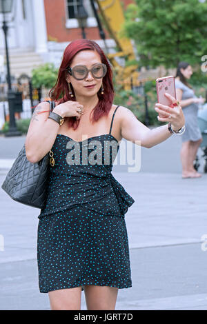 Eine attraktive Asiatin mit leuchtend roten Haaren und ein Tattoo dauert ein Selbstporträt im Washington Square Park in Greenwich Village in New York City Stockfoto