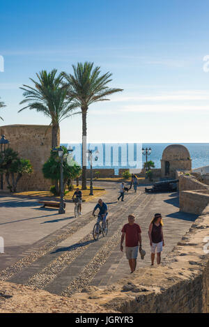 Sardinien Alghero Hafen, an einem Sommertag am Nachmittag radeln oder spazieren Sie entlang der mittelalterlichen Stadtmauer von Meer im Hafen von Alghero, Sardinien, Italien. Stockfoto