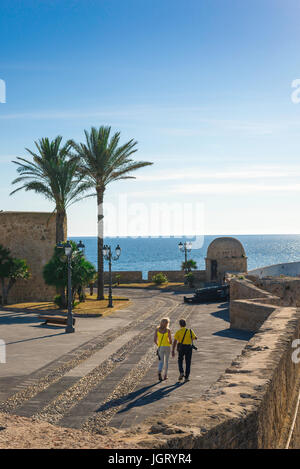 Paare mediterraner Urlaub, Rückansicht eines Mannes und einer Frau, die auf der mittelalterlichen Ufermauer im malerischen Hafengebiet von Alghero, Sardinien, Italien spazieren. Stockfoto