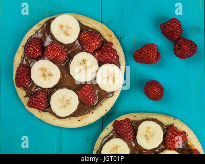 Pfannkuchen mit Nutella mit Banane und Himbeeren auf blauem Grund Stockfoto