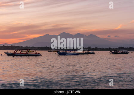 Boote im Hafen im Vordergrund bei Sonnenaufgang mit Bergen im Hintergrund auf Gili Trawangan Hafen, in der Nähe von Bali Stockfoto