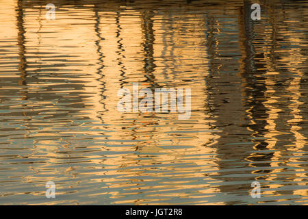 Reflexion eines Piers in den Wassern des Sees erstellt durch das Licht der untergehenden Sonne bilden unterschiedlicher Größe und Form der Schimmer und Farben Stockfoto