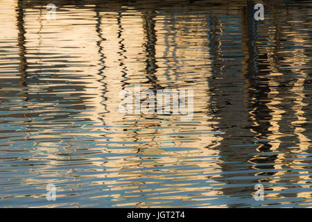 Reflexion eines Piers in den Wassern des Sees erstellt durch das Licht der untergehenden Sonne bilden unterschiedlicher Größe und Form der Schimmer und Farben Stockfoto