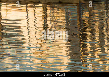 Reflexion eines Piers in den Wassern des Sees erstellt durch das Licht der untergehenden Sonne bilden unterschiedlicher Größe und Form der Schimmer und Farben Stockfoto