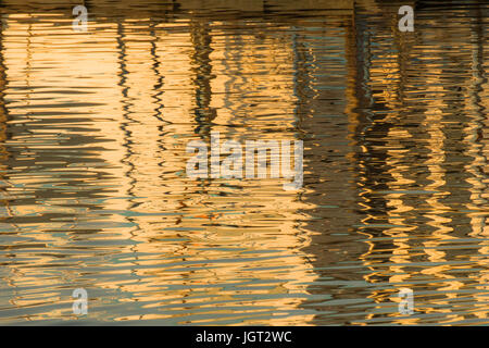 Reflexion eines Piers in den Wassern des Sees erstellt durch das Licht der untergehenden Sonne bilden unterschiedlicher Größe und Form der Schimmer und Farben Stockfoto