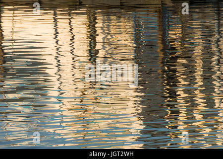 Reflexion eines Piers in den Wassern des Sees erstellt durch das Licht der untergehenden Sonne bilden unterschiedlicher Größe und Form der Schimmer und Farben Stockfoto