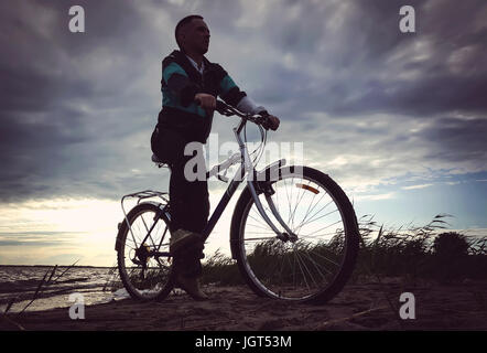 Ein Mann reitet auf seinem Mountainbike am Strand. Der Kerl am Strand Reiten, mit dem Fahrrad in der Nähe des Sees Stockfoto