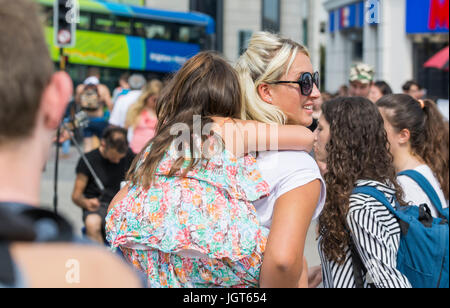 Junge Mutter mit ihrer kleinen Tochter auf ihr Rücken durch Massen in einer überfüllten Stadt. Stockfoto