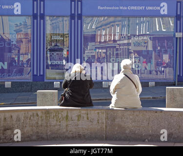 Paisley Schottland Freunde auf einer Bank an einem sehr sonnigen Tag, der Hauptstraße vor der lokalen Credit union Stockfoto