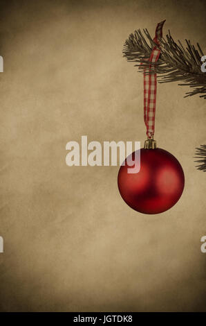 Eine Rote Christbaumkugel Frame, einem bunten Pergament Papier Hintergrund rechts von einem Weihnachtsbaum Zweig hängen. Textfreiraum links und b Stockfoto