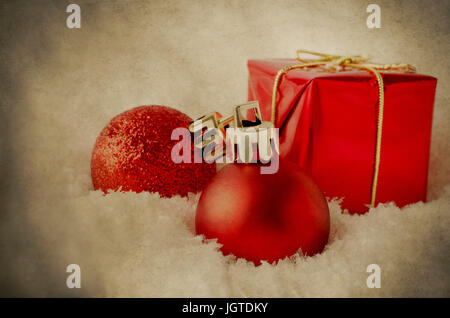 Eine Anordnung der roten Weihnachtsschmuck, weichen, weißen künstlichen Schnee zu versinken. Verarbeitet, um eine verwitterte, Grunge, Vintage aussehen zu verleihen. Stockfoto