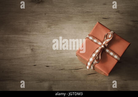 Eine quadratische Geschenkbox schräg gesetzt und gebunden mit Gingham Check Band, Schüsse von oben aufs geplankte Holztisch.  Vintage-Stil Färbung und vignette Stockfoto