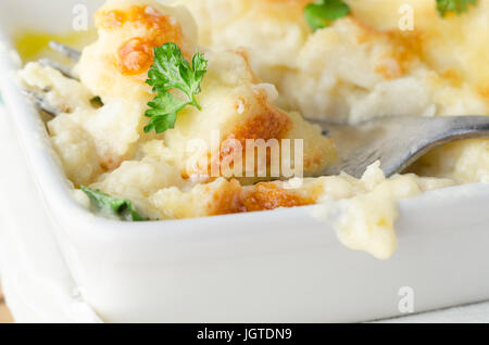 Gastro-Szene. Nahaufnahme eines Gerichts des goldenen gebackenen Blumenkohl-Käse mit Gabel eingefügt.  Mit frischer Petersilieblätter verstreut und ruht auf einem weißen c Stockfoto