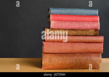 Schuss von einem Haufen von alten, schäbig, gut gebrauchte Lehrbücher gestapelt in einem Stapel auf dem Schreibtisch vor einer schwarzen Tafel in der Nähe.  Kopieren Sie Platz auf der linken Seite. Stockfoto