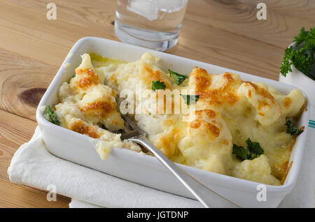 Mahlzeit auf einem Holzbrett Tisch Kiefer gesetzt.  Eine Schüssel mit goldenen gebackenen Blumenkohl Käse, verstreut mit frischer Petersilie Blätter.  Silberne Gabel eingefügt wie wenn Dini Stockfoto