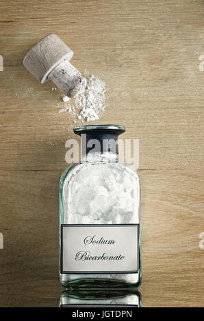 Ein Vintage-Stil Flasche Natriumbicarbonat (Natron) auf glänzend reflektierende Holzoberfläche.  Cork geöffnet und Pulver verstreut. Stockfoto