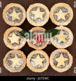 Hausgemachte Weihnachten Mince Pies mit Blätterteig Sterne und Puderzucker bestäuben, Holly und rote Beeren auf Eiche Holz Hintergrund. Stockfoto