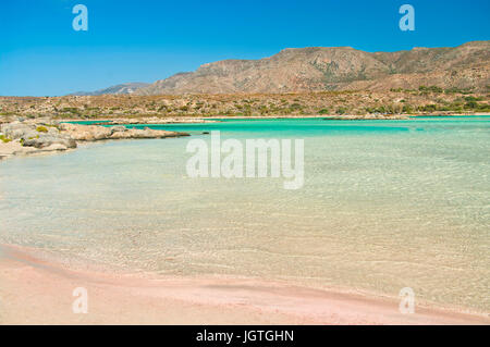 klar, seichtem Wasser umspült am berühmten Strand von Elafonisi mit rosa Sand und Berge im Hintergrund auf Kreta an sonnigen Sommertag, Stockfoto