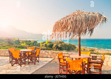 zwei Tabellen mit einer Palme lassen Sonnenschirm auf Restaurant-Balkon mit Meer- und Bergblick in frühen Morgenstunden, Falasarna Strand, Kreta, Griechenland Stockfoto