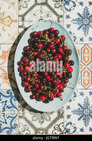 Frische reife Süßkirschen in blaue Platte über farbenfrohe orientalische Fliesen Hintergrund, Draufsicht, flach zu legen. Sommer-Food-Konzept Stockfoto