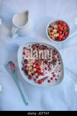 Schoko-Müsli mit Mandelmilch und roten & weiße Johannisbeeren in einer weißen Schüssel Stockfoto