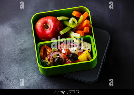 Griechischer Salat essen und Apfelfrucht in Lunchpaket auf Tafel Hintergrund herausnehmen Stockfoto