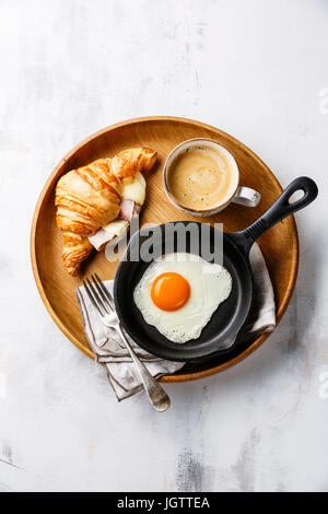 Frühstück mit Spiegelei auf Eisenpfanne, Croissant-Sandwich mit Käse und Schinken und Kaffee auf Holztablett auf weißem Hintergrund Stockfoto