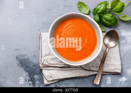 Tomatensuppe Gazpacho in Schüssel und grüner Basilikum auf grauem Beton Hintergrund Stockfoto