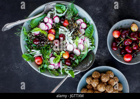 Kirsche Wildreis-Salat mit Hibiskus-Vinaigrette serviert mit Weißwein.  Auf schwarz/grau Hintergrund fotografiert. Stockfoto