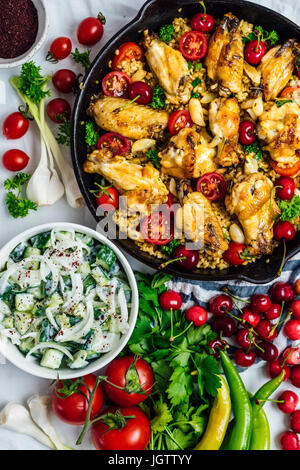 Chicken Wings und Bulgur-Pilaw gekocht in einer Pfanne, garniert mit Kirschen, Cherry-Tomaten und Kräuter aus der Ansicht von oben fotografiert. Stockfoto