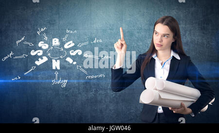 Frau in einem Anzug in der Nähe von Wand mit Blaupausen und ein Geschäft Ideenskizze drauf gezogen. Konzept eines erfolgreichen Unternehmens. Stockfoto