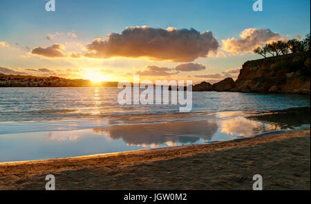 Sonnenuntergang über kleine Stadt vom Sandstrand mit kleinen Felseninsel rechts, Kreta, Griechenland Stockfoto