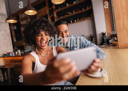 Glückliches junges Paar beisammen sitzen im Café und nehmen Selfie mit Handy. Afrikanerin mit ihrem Freund unter Selbstbildnis mit intelligenten pho Stockfoto