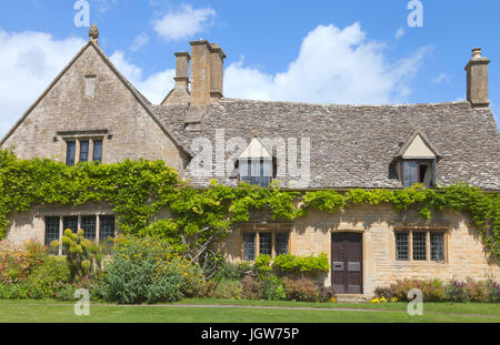 Charmantes altes Steinhaus mit Klettern Glyzinien an die Wand und Blumen, Sträucher im Vorgarten, an einem sonnigen Sommertag. Stockfoto