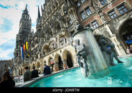 München, Deutschland - 9. Mai 2017: Menschen sitzen am Rande der Fischbrunnen mit neuen Rathaus im Hintergrund am Marienplatz in München. Stockfoto