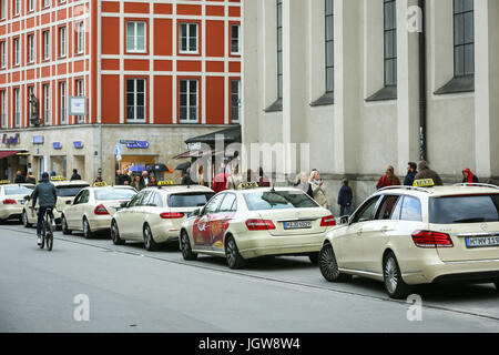 München, Deutschland - 9. Mai 2017: Passanten auf der Straße neben dem aufgereiht geparkten Taxis mit einem Radfahrer in München vorbei. Stockfoto