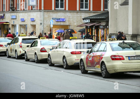 München, Deutschland - 9. Mai 2017: Passanten auf der Straße neben dem aufgereiht geparkten Taxis in München. Stockfoto