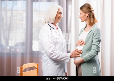 grauen Haaren Arzt und jungen schwangeren Bauch während ärztliche Beratung zu halten Stockfoto