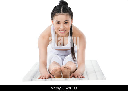 lächelnden Asiatin in Sportbekleidung üben nach vorne beugen Pose auf Yogamatte isoliert auf weiss Stockfoto