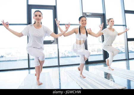 Lächelnde junge Frauen üben Garudasana Adler darstellen, im Yoga-Kurs Stockfoto