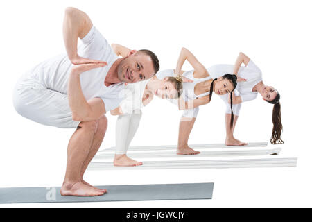 Junge Frauen mit Trainer üben drehte Stuhl-Yoga-Pose auf Matten Stockfoto