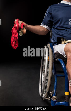 verkürzte Ansicht der Paralympischen im Rollstuhl sitzen und halten Goldmedaillen isoliert auf schwarz Stockfoto