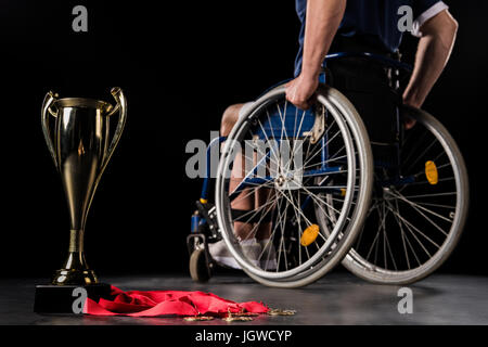 zugeschnittenen Überblick Paralympic Rollstuhl gehen weg von seinem Meister Becher und Goldmedaillen isoliert auf schwarz Stockfoto