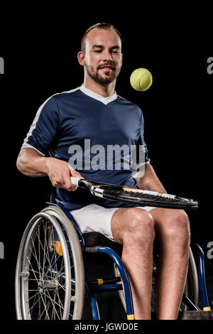 Behinderte junge Sportler im Rollstuhl sitzen und Tennisspielen isoliert auf schwarz Stockfoto