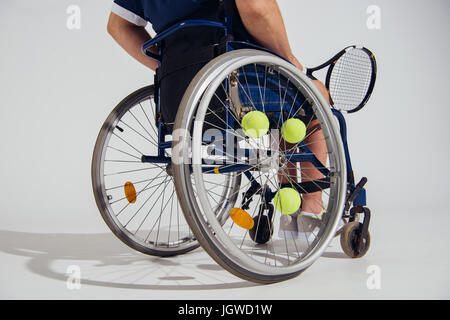 verkürzten Blick auf Tennisspieler sitzt im Rollstuhl mit Tennisschläger und Bällen auf grau isoliert Stockfoto