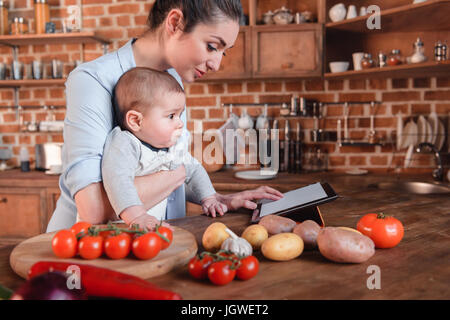 Mutter mit ihrem Baby Sohn auf der Suche nach Rezept auf digital-Tablette vor dem Abendessen in der Küche kochen Stockfoto
