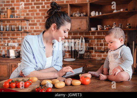 Mutter mit ihrem Baby Sohn auf der Suche nach Rezept auf digital-Tablette vor dem Abendessen in der Küche kochen Stockfoto
