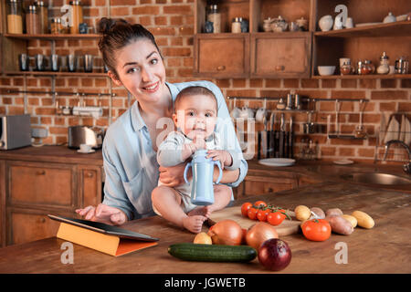 Porträt der jungen Mutter mit ihrem kleinen Sohn kochen Abendessen zusammen und mit digital-Tablette in der Küche Stockfoto